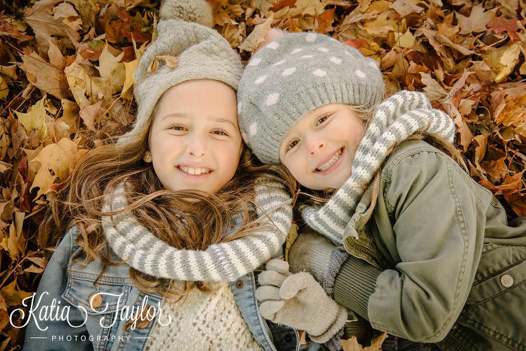 Sisters lying in the red and orange leave in Toronto High Park in the Fall.