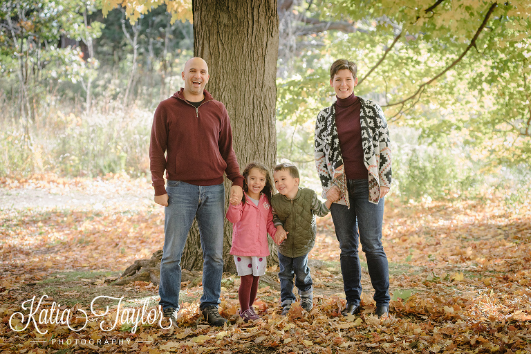 Family hold hands in the Fall leaves in Toronto High Park.