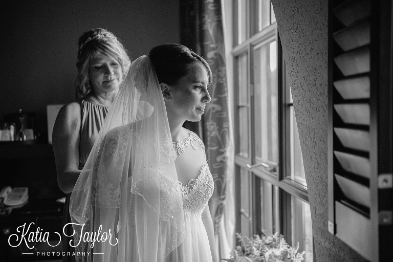 Bride looks out of window as bridesmaid helps her with her wedding dress. The Old Mill in Toronto.