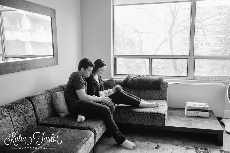 New parents in living room with baby on their lap. Toronto lifestyle newborn portraits. www.katiataylorphotography.com