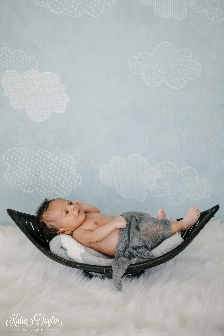 Baby boy lying on a basket with illustrated cloud backdrop. Toronto newborn portraits.