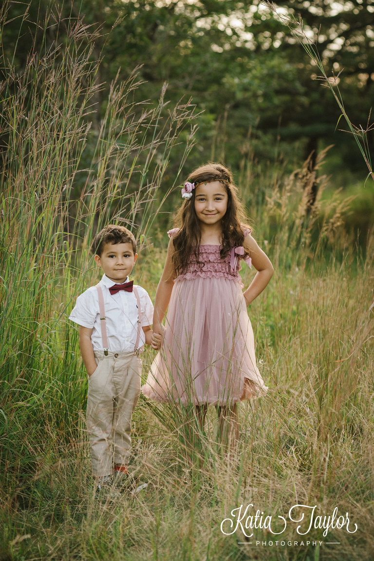 Brother and sister hold hands in tall grass. Toronto family portraits in High Park. 