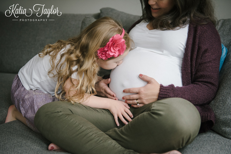 Little girl kisses her pregnant mother's belly. Toronto maternity portraits at home.