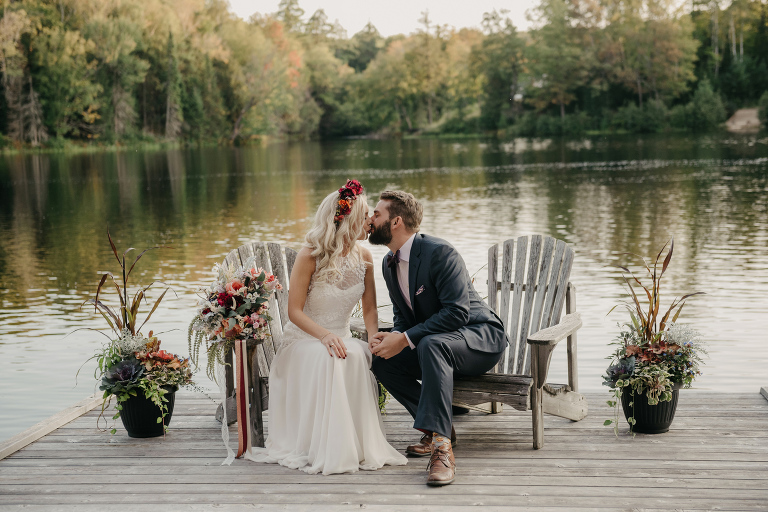 Bride and groom kiss on the dock in Muskoka chairs. Haliburton Ontario wedding. Rustic country wedding.