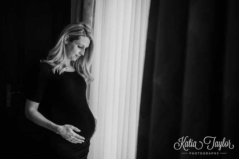 Pregnant woman in black dress by the window. Toronto lifestyle maternity portraits.