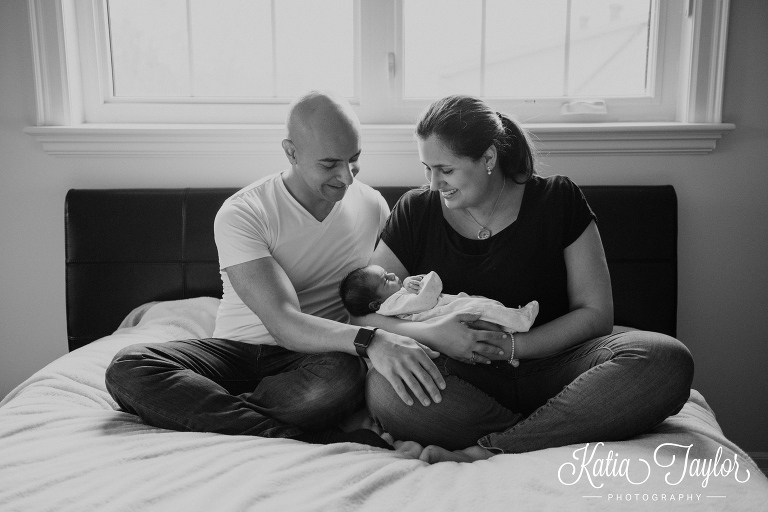 Parents sitting on the bed with their newborn baby. Toronto lifestyle newborn portraits.