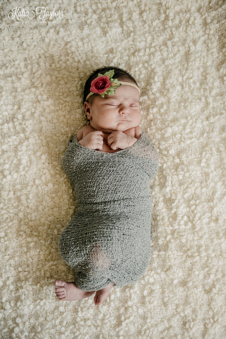 A sleeping newborn baby girl with a pink flower headband wrapped in a grey stretchy wrap. Toronto newborn photography.