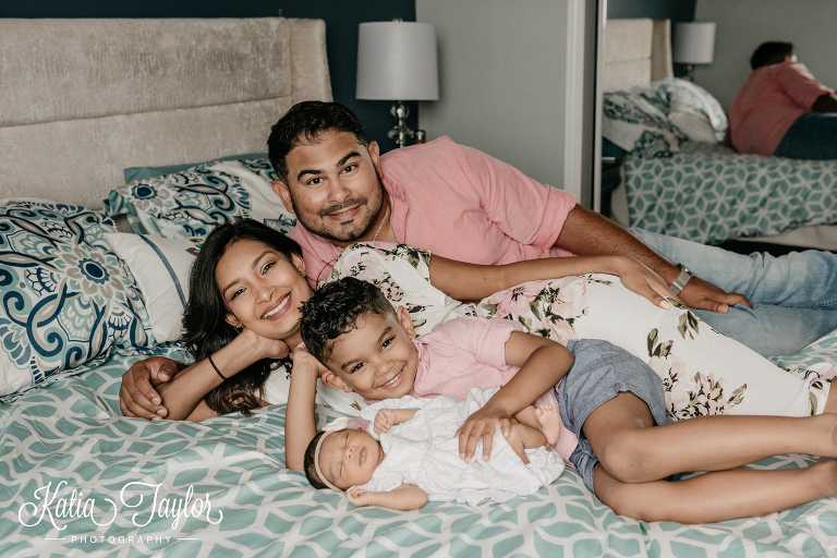 A family of four laying on the bed with their newborn baby girl. Toronto newborn photography.