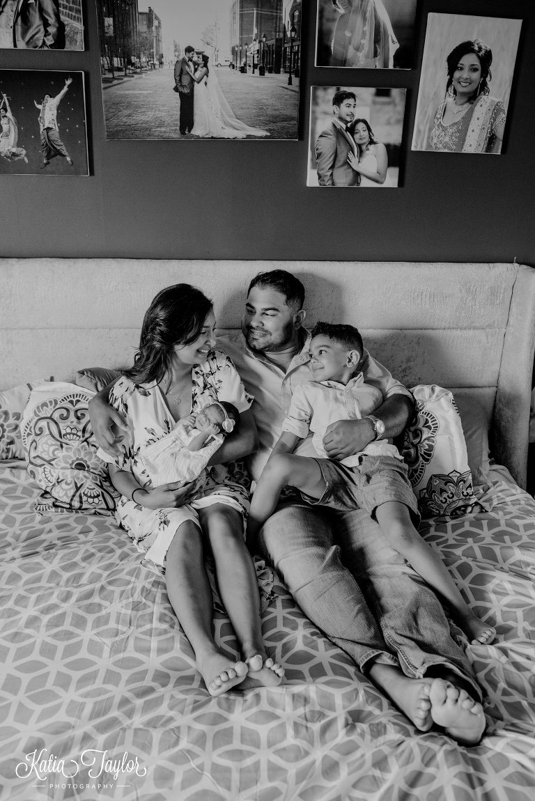 A family of four with a newborn baby girl snuggling together on the bed. Toronto newborn photography.
