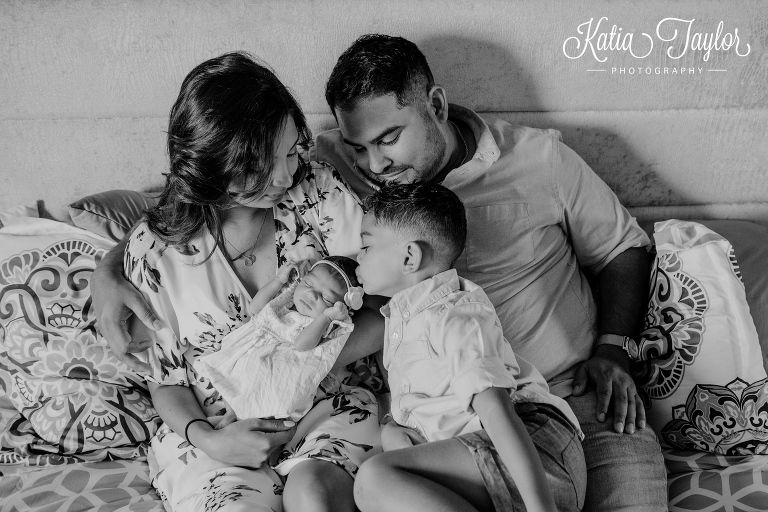 A new big brother kisses his newborn baby sister on the head as parent smile. Toronto newborn photography.