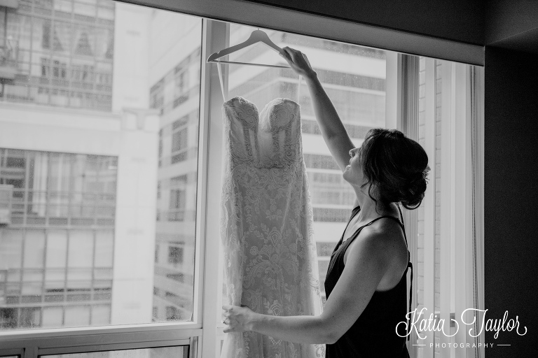 A bride reaching for her wedding dress as it's hanging in the window. Toronto wedding photography.