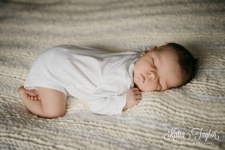 A sleeping baby in a white onesie laying on a yellow and white blanket. Toronto newborn portraits.