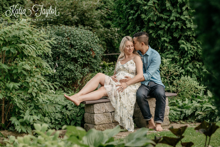 Pregnant couple sitting on a stone bench in a beautiful green garden. Toronto maternity photography.