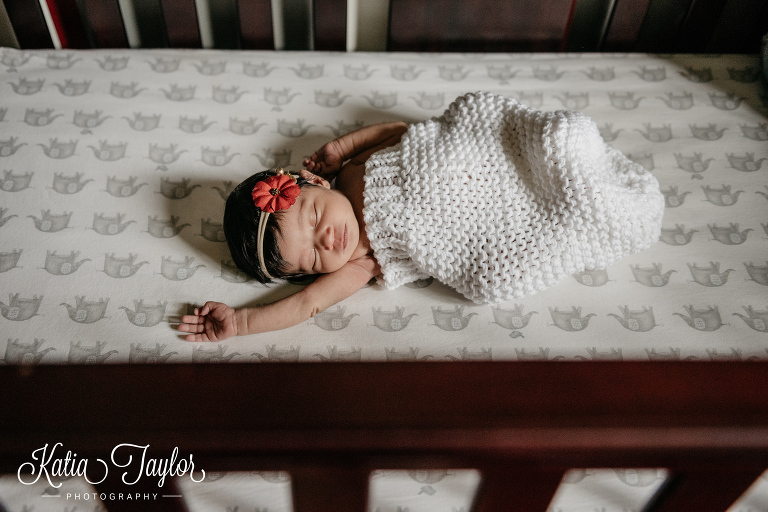 Newborn baby girl stretching her arms while asleep in her crib. Toronto newborn portraits.