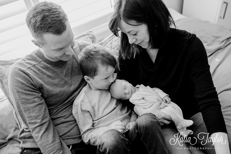 Family sitting on a couch as big brother kisses his newborn sister's head