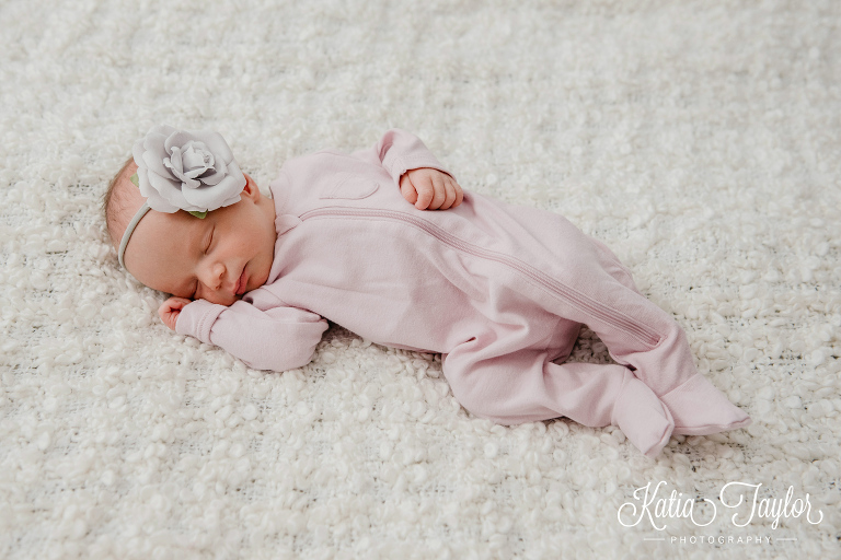 A newborn baby girl in a pink sleeper with a grey flower headband