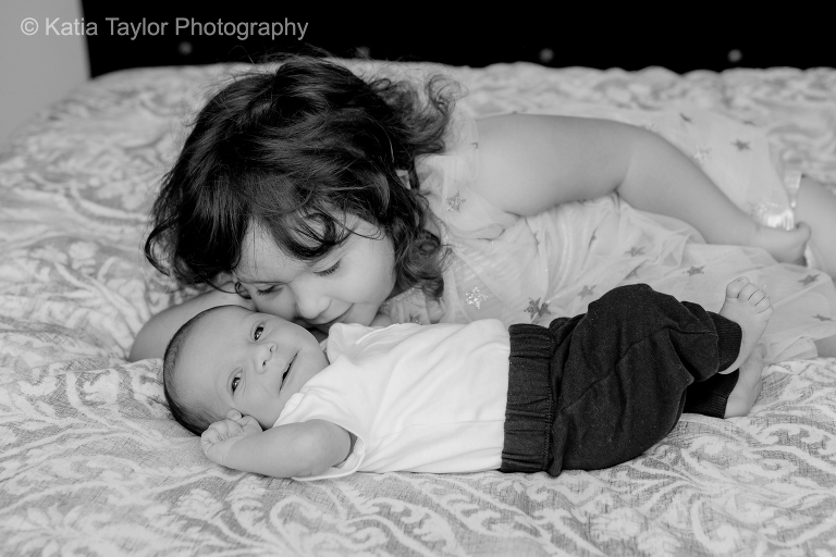 Newborn baby boy gets a kiss on the cheek from his toddler big sister
