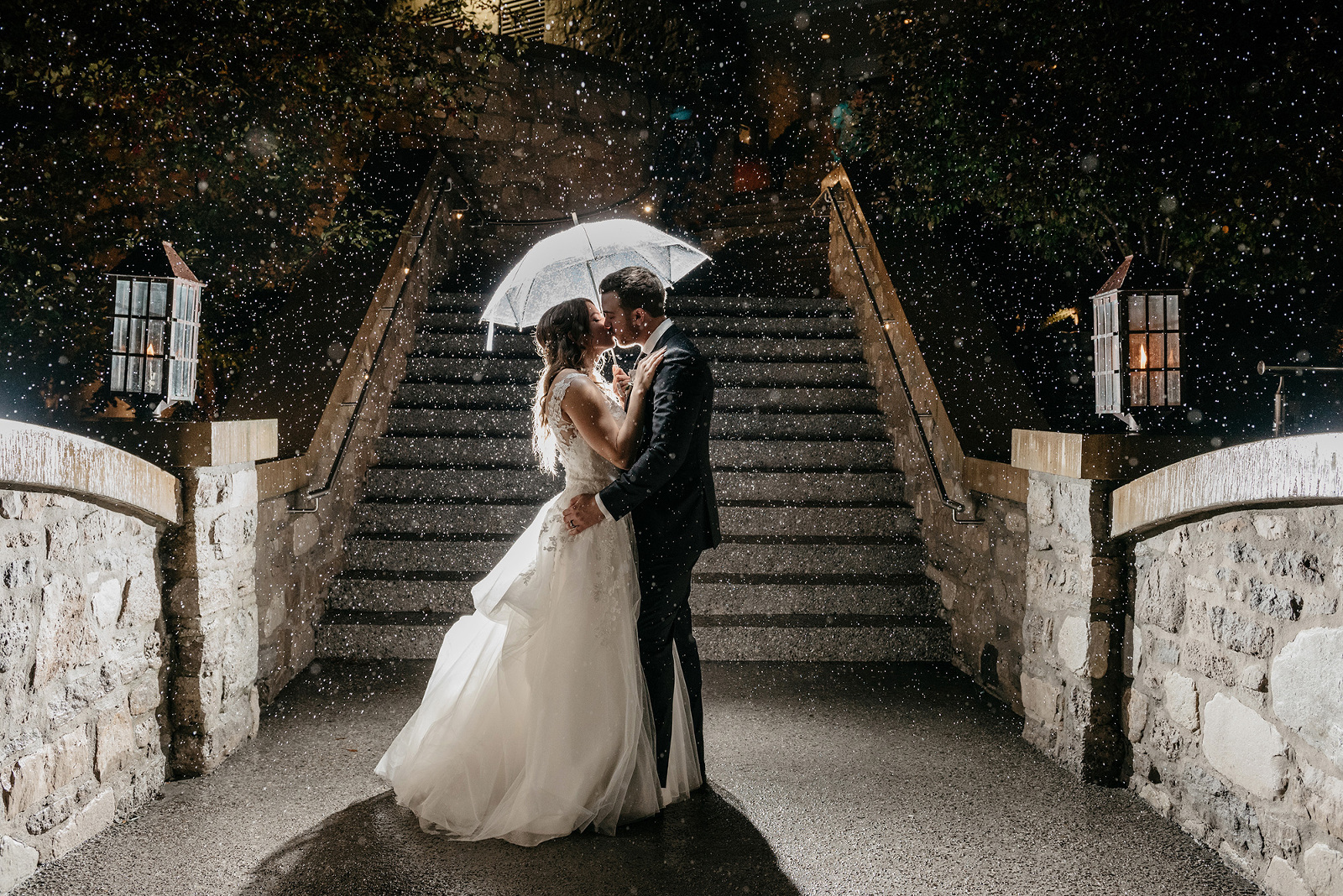 Bride and groom kiss under an umbrella in the rain at night at Ancaster Mill, Ontario