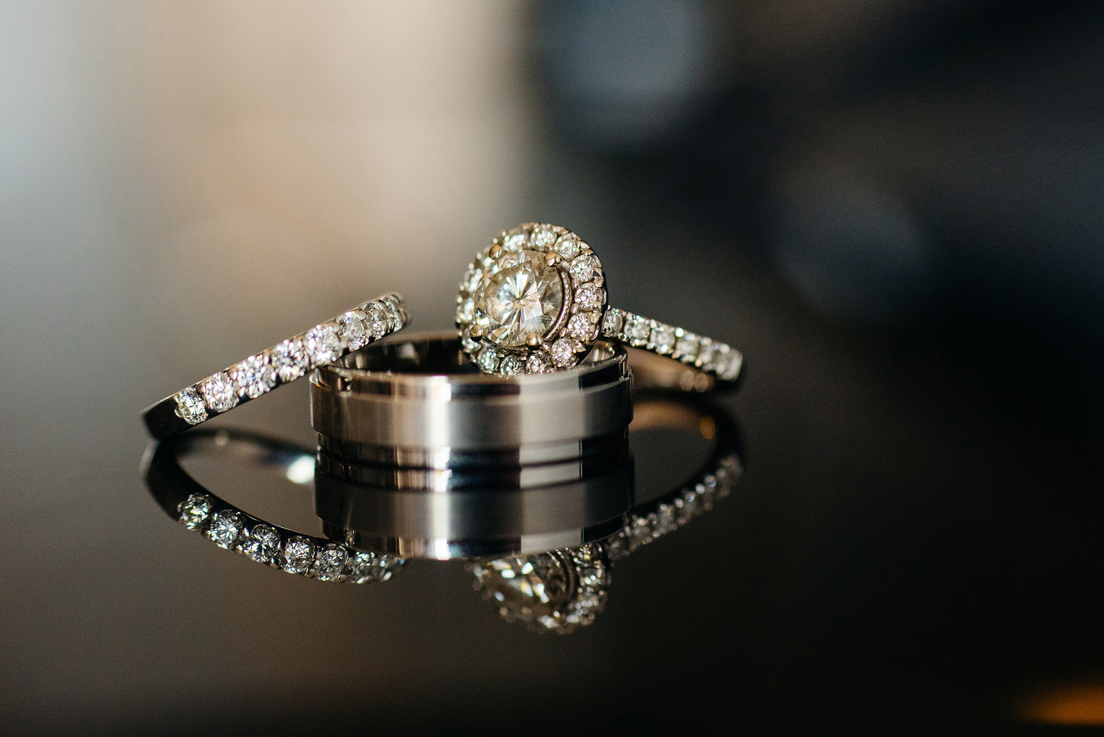 Two wedding rings and a diamond engagement ring on a reflective surface