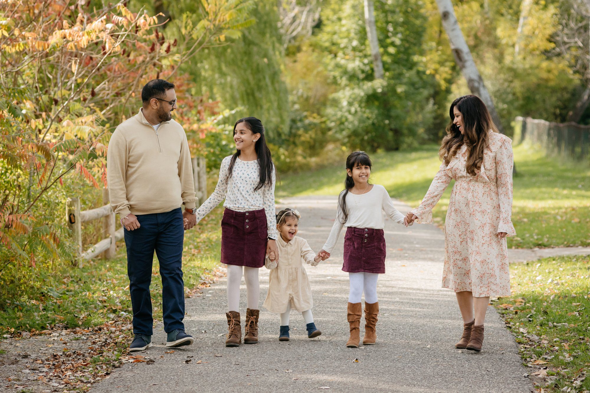 Husband and wife with their three small girls walking a path through a park during the fall time