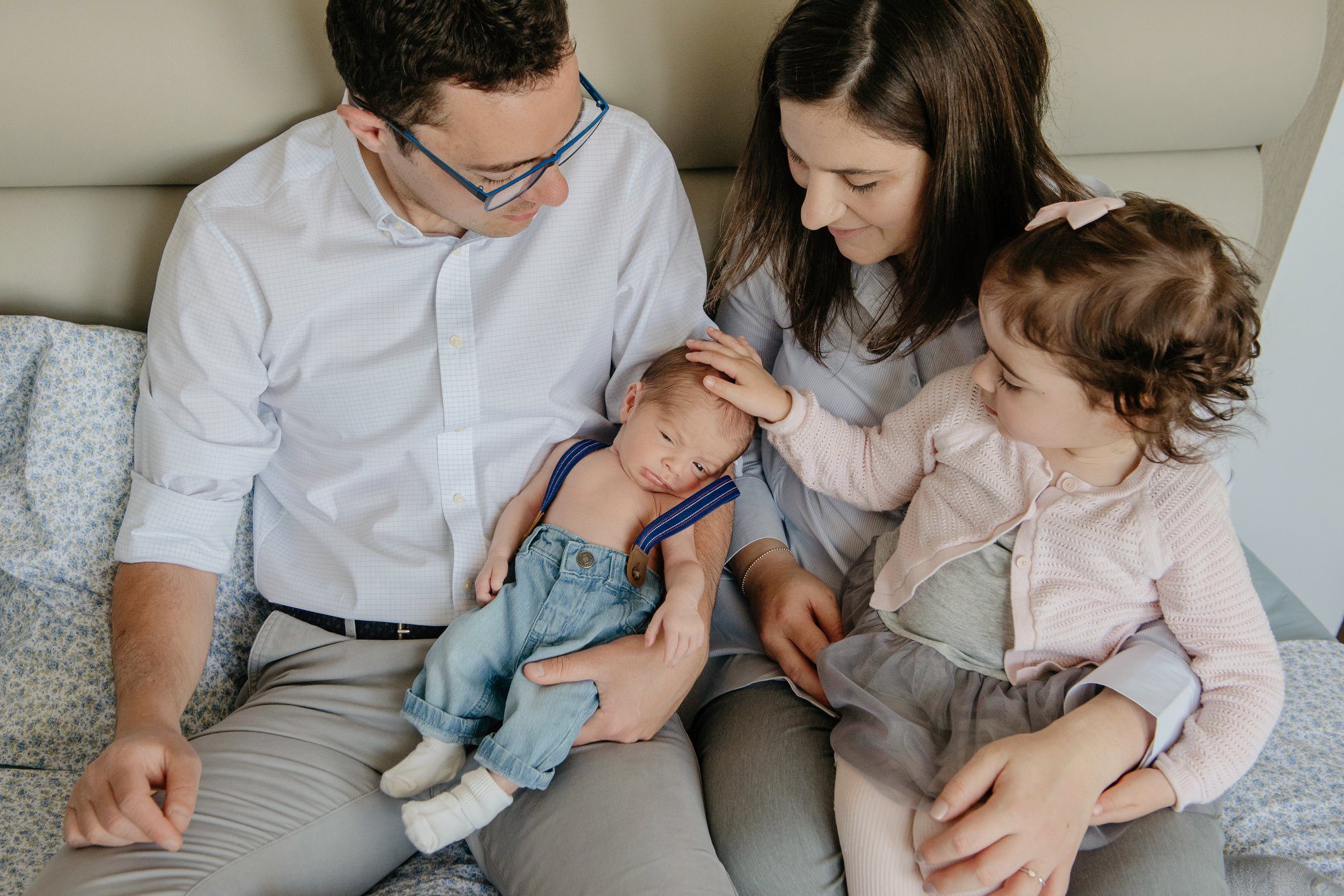 Big sister rubs the hair of her newborn baby brother has her parents watch on