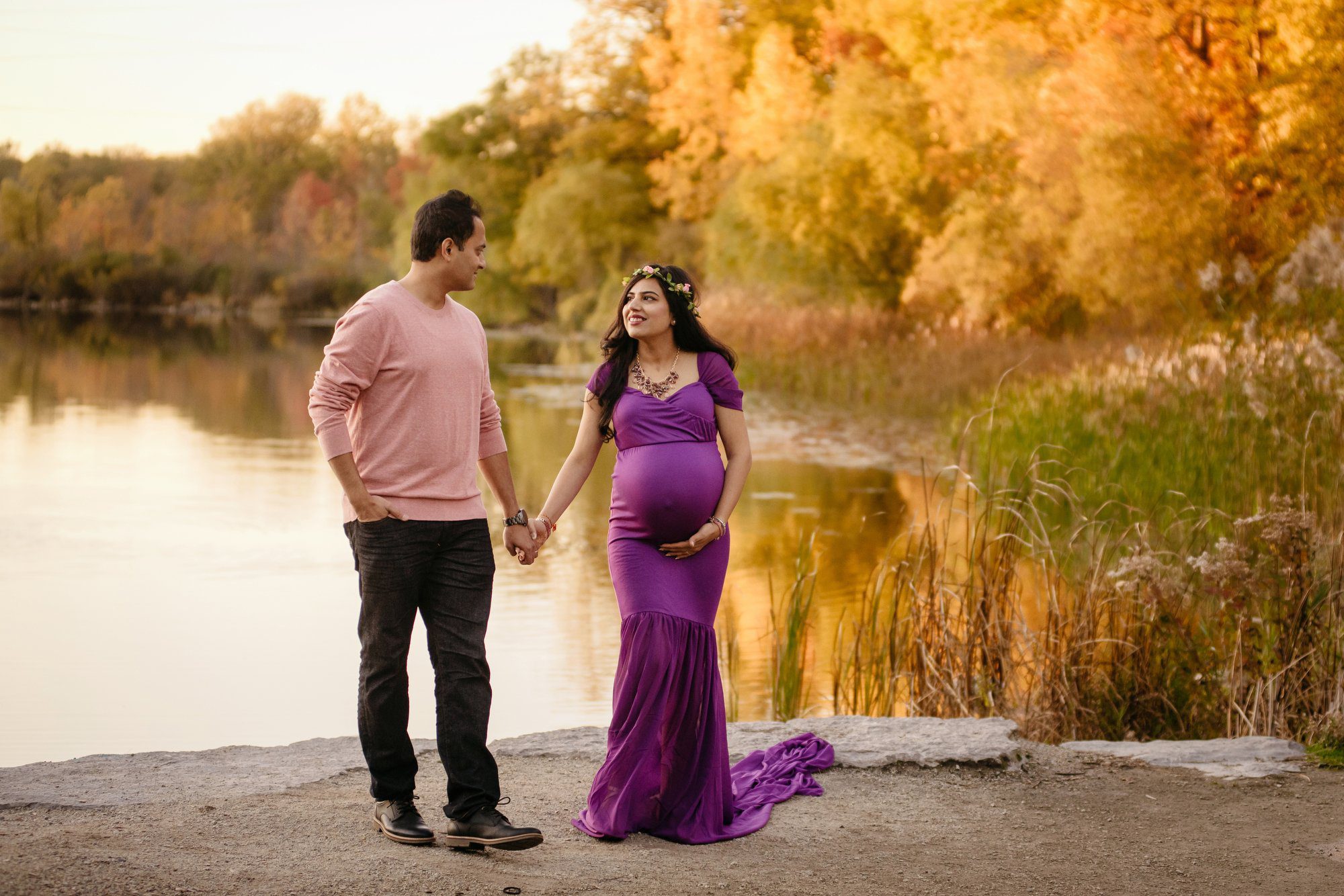 Pregnant woman in a beautiful purple gown and flower crown walking with her husband surrounded by fall colours